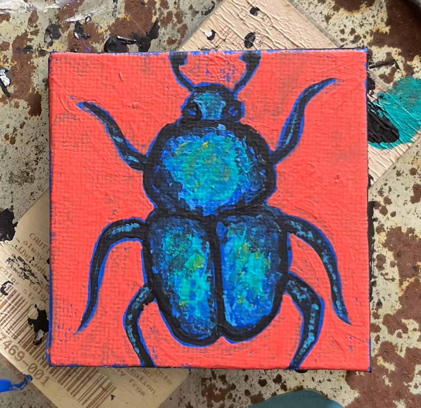 Mini Bug — original 2.44 inch caulk texture mini painting by Jay the Painter, Akron Ohio. Bold blue teal beetle with iridescent wings on vivid coral red background. SOLD.