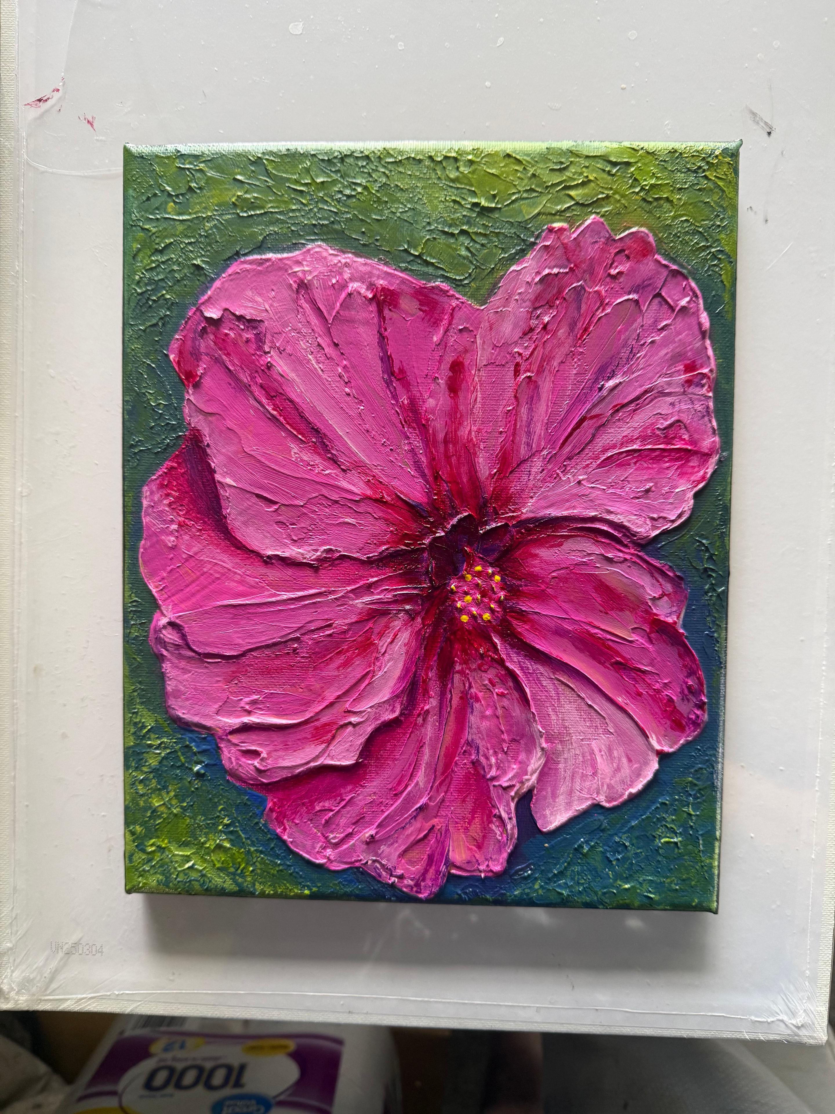 Mom's Garden Flower — original 8x10 inch caulk art floral painting by Jay the Painter, Akron Ohio. Vibrant pink hibiscus flower with thick 3D caulk texture petals, yellow stamen center, on a green and blue textured background. SOLD.